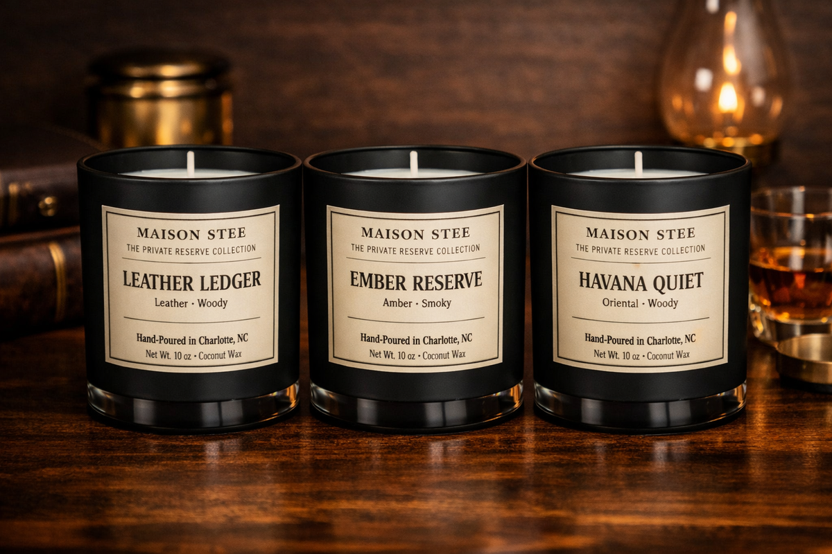 Maison Stee Private Reserve Collection candles on a dark wooden surface with warm, moody lighting. Elegant props in the background create a refined, intimate atmosphere. Text reads ‘Private Reserve Collection.'