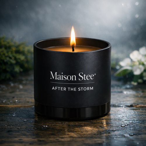 Maison Stee After the Storm candle burning in a glass matte‑black vessel on a damp wooden surface. Cool misty light, dewdrops, and soft natural textures create a serene, post‑rain atmosphere.