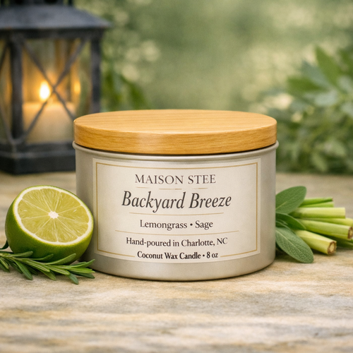 Maison Stee Backyard Breeze candle lit on a wooden surface with fresh outdoor accents and bright, airy lighting.