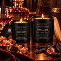 Maison Stee XO Reserve candles in glass matte black vessels, lit and glowing, styled beside a cognac glass, decanter, caramel pieces, aged barrel, and dried figs — Spirit House Collection.