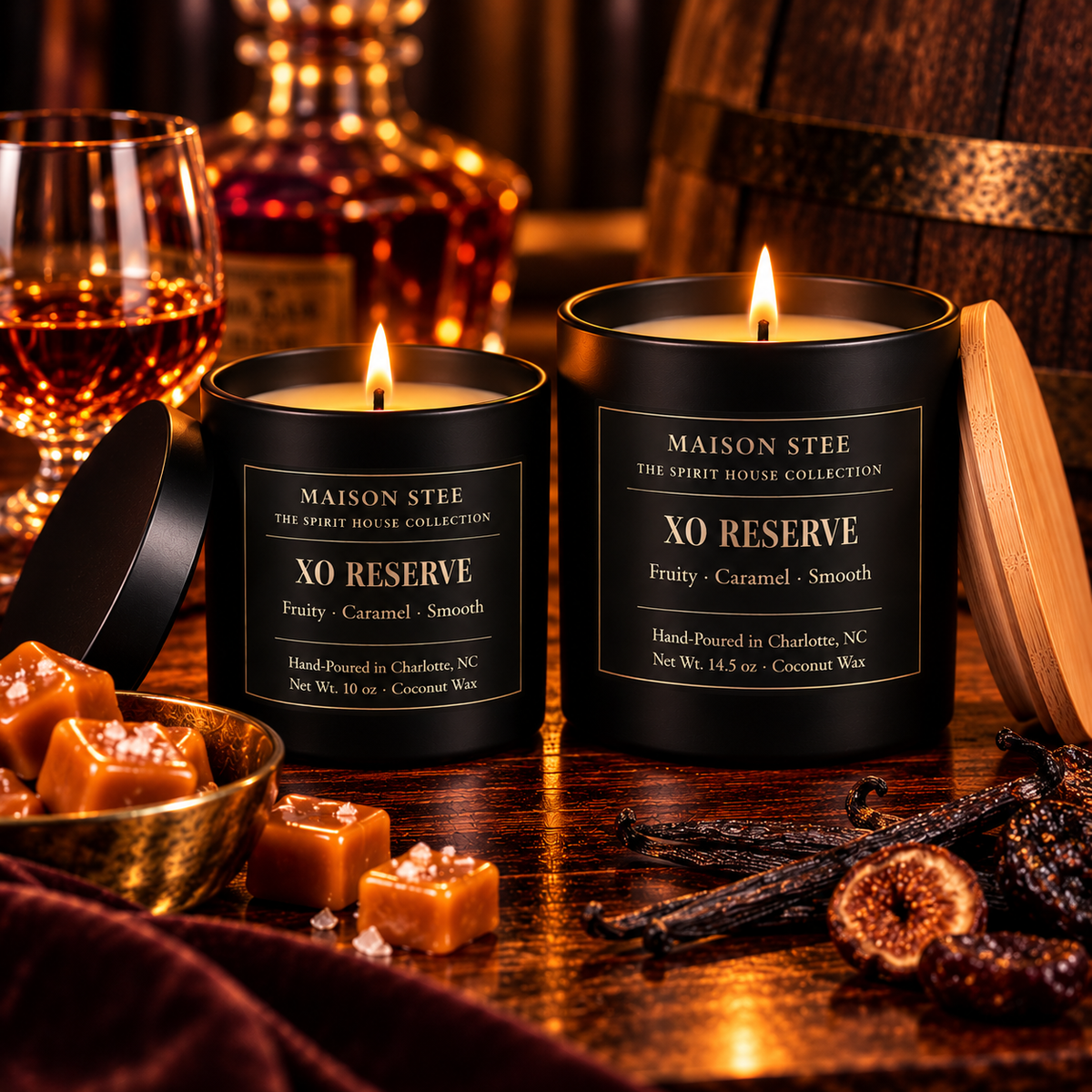 Maison Stee XO Reserve candles in glass matte black vessels, lit and glowing, styled beside a cognac glass, decanter, caramel pieces, aged barrel, and dried figs — Spirit House Collection.