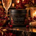 Maison Stee Cranberry Nocturne candle in a matte black tin, styled with fresh cranberries, sparkling Prosecco, burgundy autumn leaves, and warm candlelight — Burnished Hearth Collection.