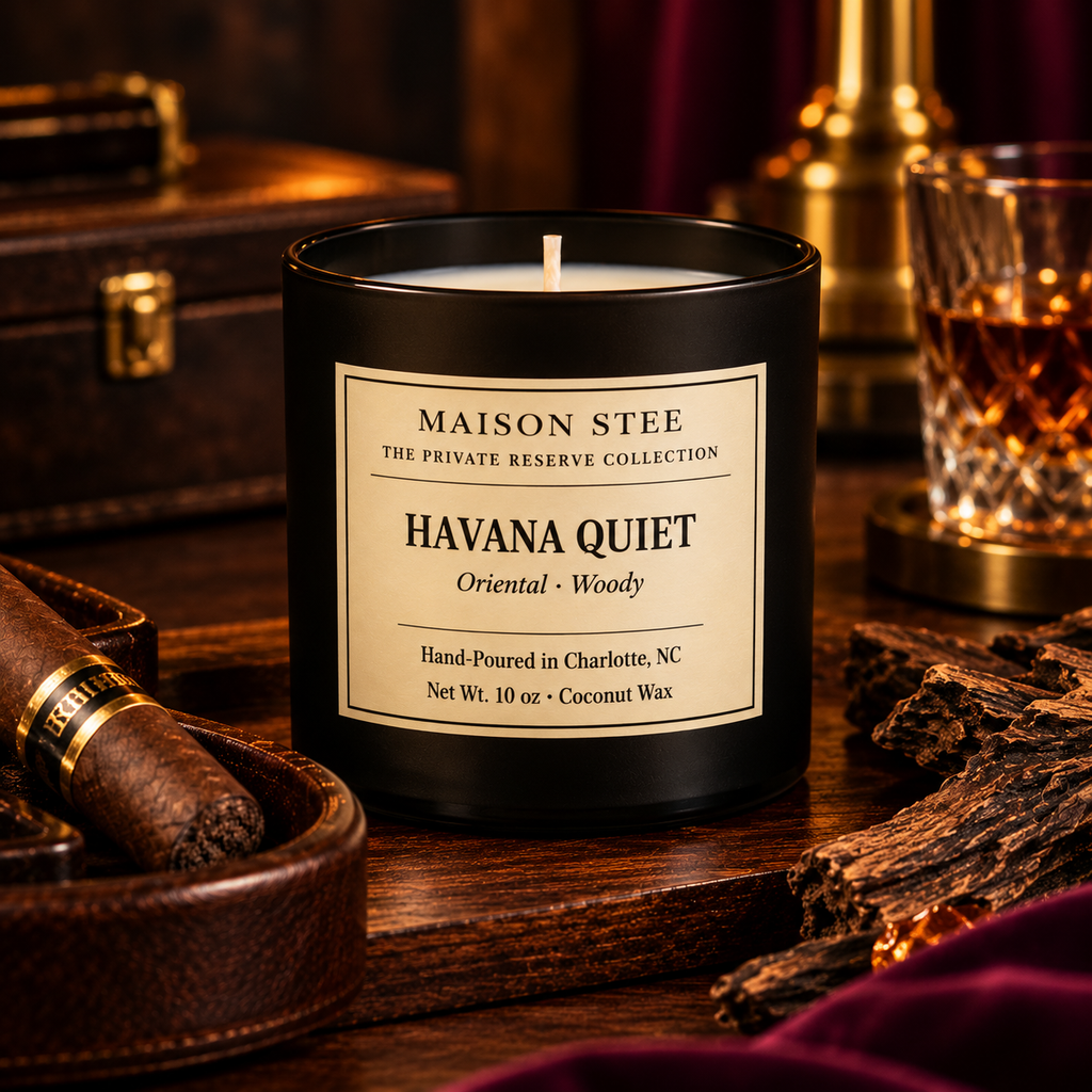 Maison Stee Havana Quiet candle candle burning softly in a glass matte‑black container with moody, warm lighting and subtle orchard‑inspired props in the background.