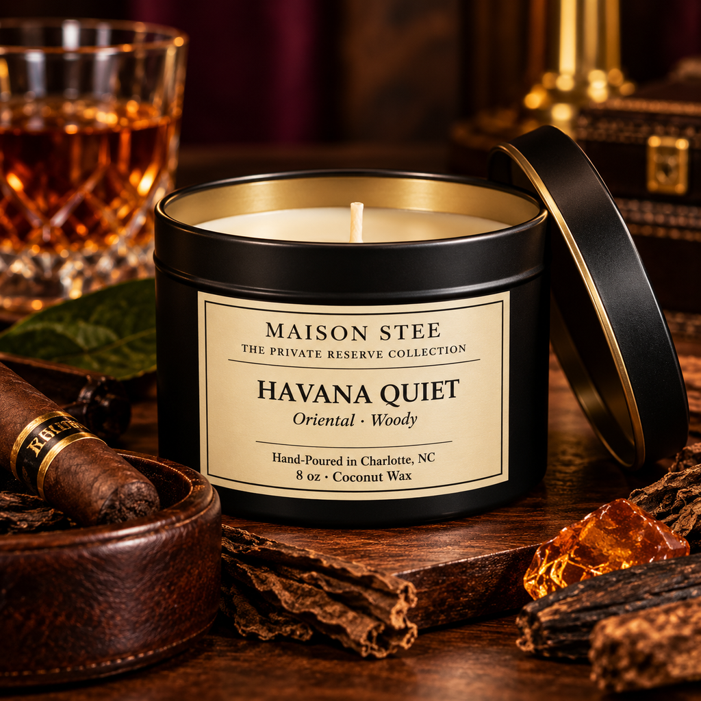 Maison Stee Havana Quiet candle candle burning softly in a tin matte‑black container with moody, warm lighting and subtle orchard‑inspired props in the background.