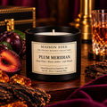 A Maison Stee 'Plum Meridian' scented candle in a matte black glass jar, styled on a rustic wooden table with fresh plums, amber liquid, and bark in the background.