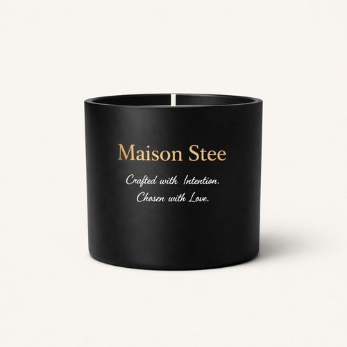 Maison Stee candle in a matte-black vessel with gold branding on a soft cream background